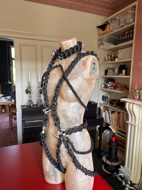 Black harness displayed on a wooden mannequin against an indoor background.
